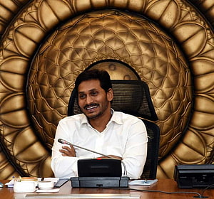 YS Jagan Mohan Reddy Seated at Conference Table with Microphone and Ornate Gold Backdrop HD wallpaper