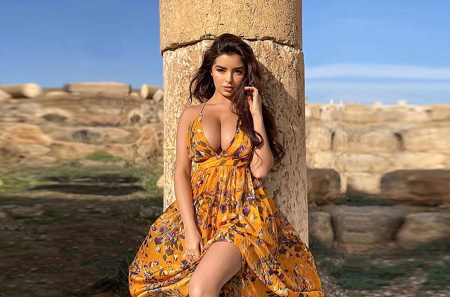 Demi Rose in a yellow floral dress leaning against a stone column at an ancient ruin HD wallpaper
