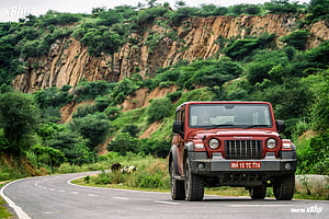 Red Mahindra Thar SUV Driving on Winding Mountain Road with Lush Green Hills HD wallpaper