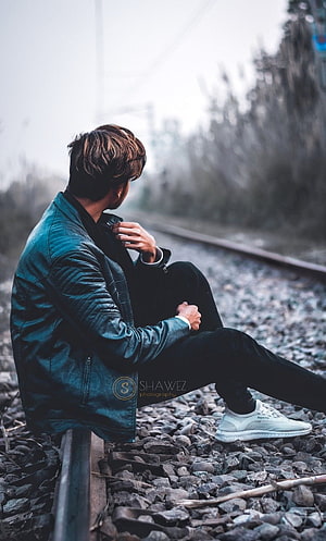 Young man in teal leather jacket sitting on railway tracks in a contemplative pose, Boys dp, sad pose boy HD phone wallpaper