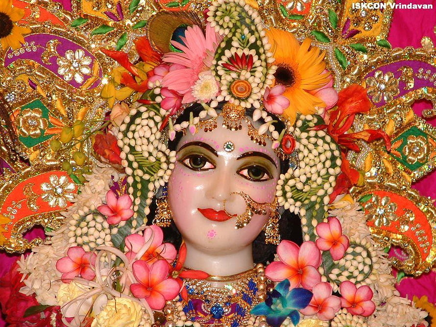 Ornate Radha Rani Murti Adorned With Vibrant Flowers And Gold Jewelry HD wallpaper