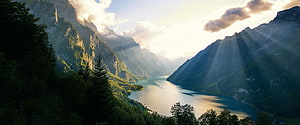 Sunbeams Over a Serene Alpine Lake Surrounded by Lush Green Mountains HD wallpaper