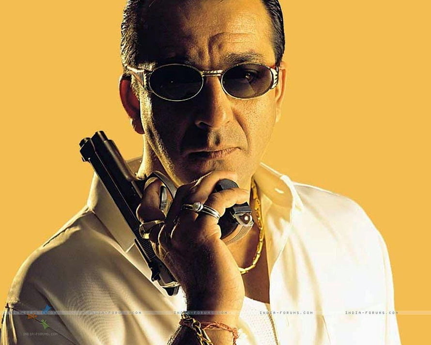 Sanjay Dutt in white shirt and sunglasses holding a pistol against a warm yellow background HD wallpaper