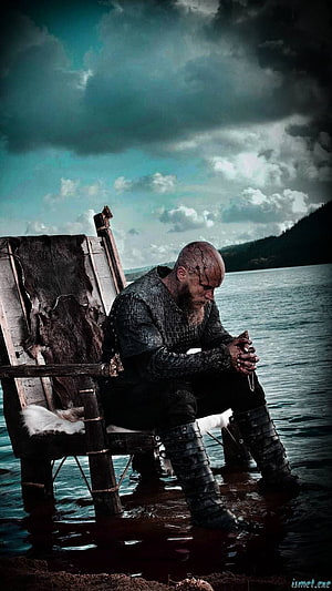 Ragnar Lothbrok seated on a wooden throne by the water in dark armor HD phone wallpaper