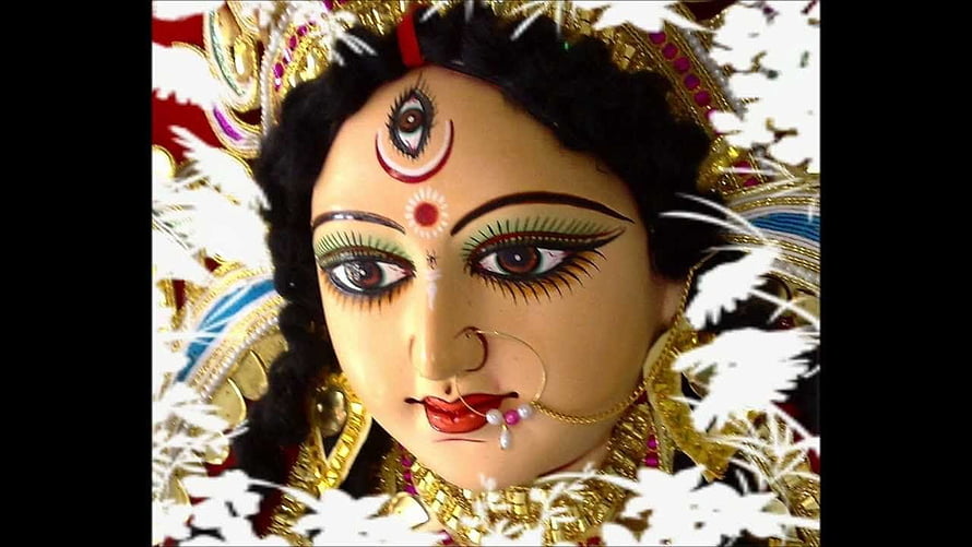Close-up of Maa Durga idol face with third eye, gold jewelry, and white floral decorations HD wallpaper