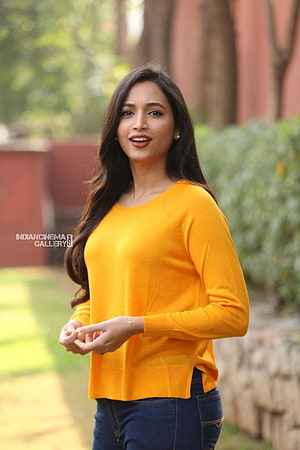 Srinidhi Shetty in a bright yellow sweater and dark jeans standing outdoors in a garden setting HD phone wallpaper