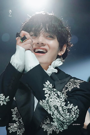 V from BTS smiling on stage in an ornate black embroidered suit with white ruffled collar HD phone wallpaper