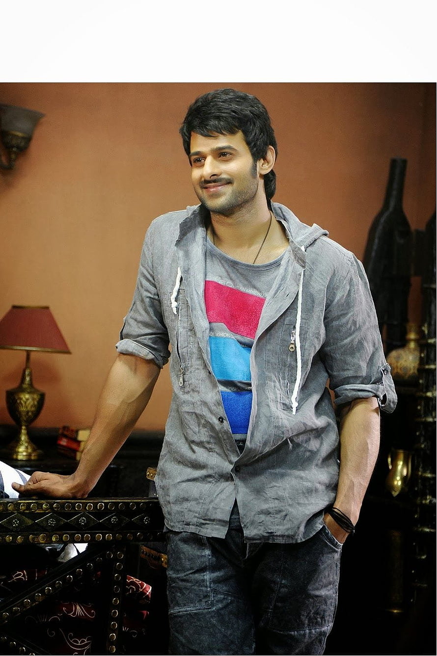 Prabhas in casual grey shirt and colorful t-shirt standing in a warmly lit interior HD phone wallpaper