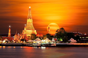 Wat Arun Temple Illuminated at Sunset Along the Chao Phraya River in Bangkok, Thailand HD wallpaper