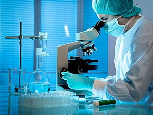 Scientist in protective gear examining samples through a microscope in a modern laboratory HD wallpaper