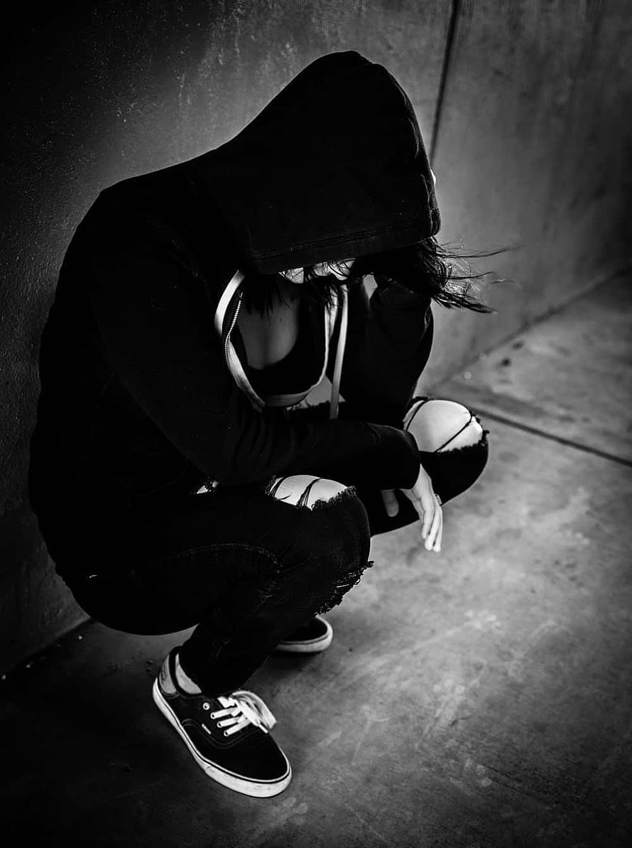 Moody Black and White Portrait of a Hooded Figure Crouching Against a Concrete Wall HD phone wallpaper