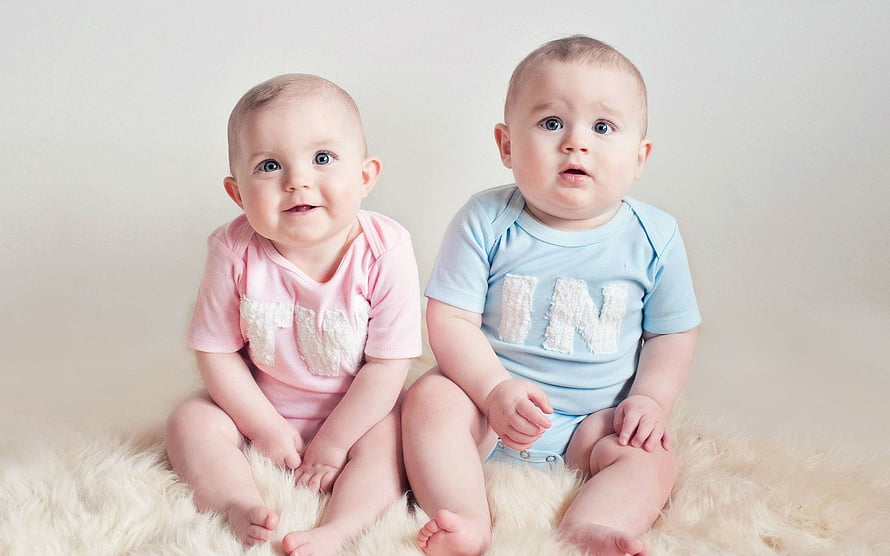 Adorable Twin Babies in Matching Pink and Blue Outfits Sitting on a Fluffy Rug HD wallpaper