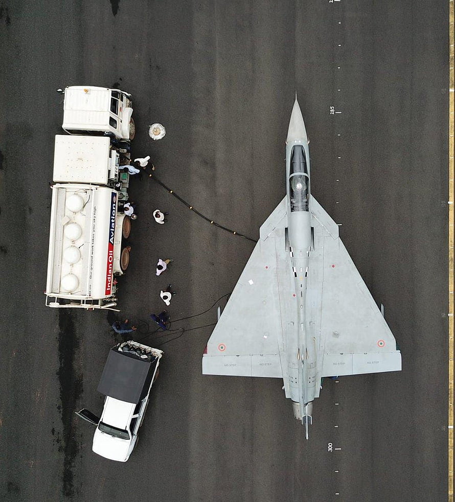 Top-down view of an LCA Tejas fighter jet on the tarmac with ground support vehicles and crew HD phone wallpaper