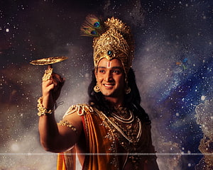 Sri Krishna in ornate golden crown and peacock feather headdress holding a discus against a starry cosmic background HD wallpaper
