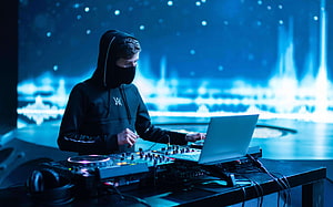 Alan Walker performing at a DJ booth with a laptop and mixer under blue stage lighting HD wallpaper