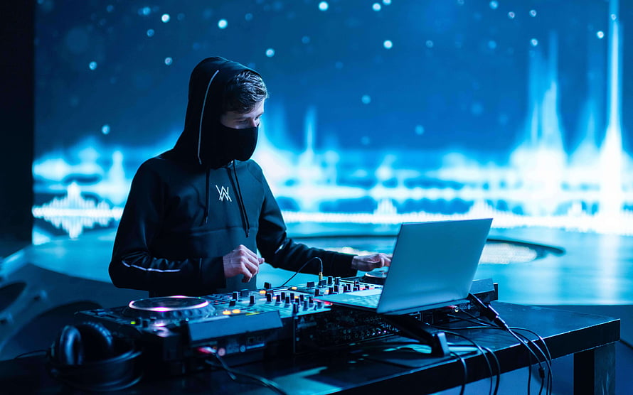 Alan Walker performing at a DJ booth with a laptop and mixer under blue stage lighting HD wallpaper