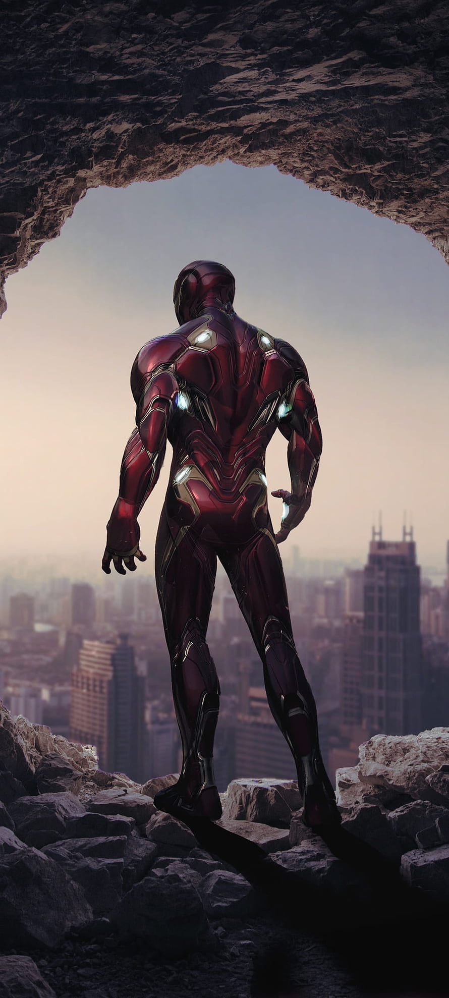 Iron Man Standing in Rocky Cave Overlooking City Skyline at Dusk HD phone wallpaper