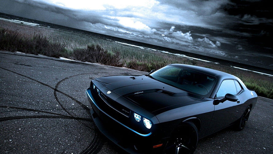 Black Dodge Challenger SRT parked on coastal road under dramatic storm clouds HD wallpaper