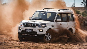 White Mahindra Scorpio SUV kicking up dust on a rugged off-road dirt track HD wallpaper