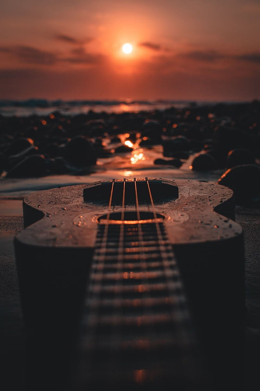 Acoustic Guitar Resting on a Rocky Shore During a Golden Sunset HD phone wallpaper