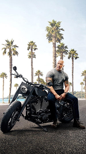 Dwayne Johnson on a black custom motorcycle with palm trees and ocean in the background HD phone wallpaper