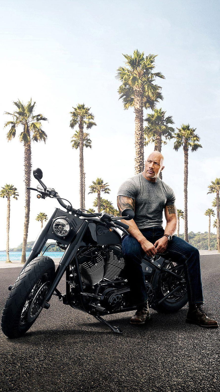 Dwayne Johnson on a black custom motorcycle with palm trees and ocean in the background HD phone wallpaper