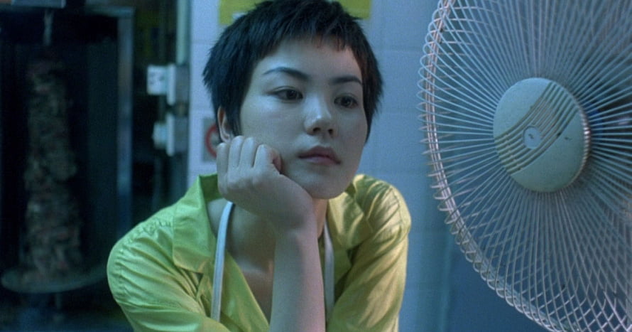 Chungking Express cinematic still of a pensive woman in a yellow shirt beside a vintage fan HD wallpaper