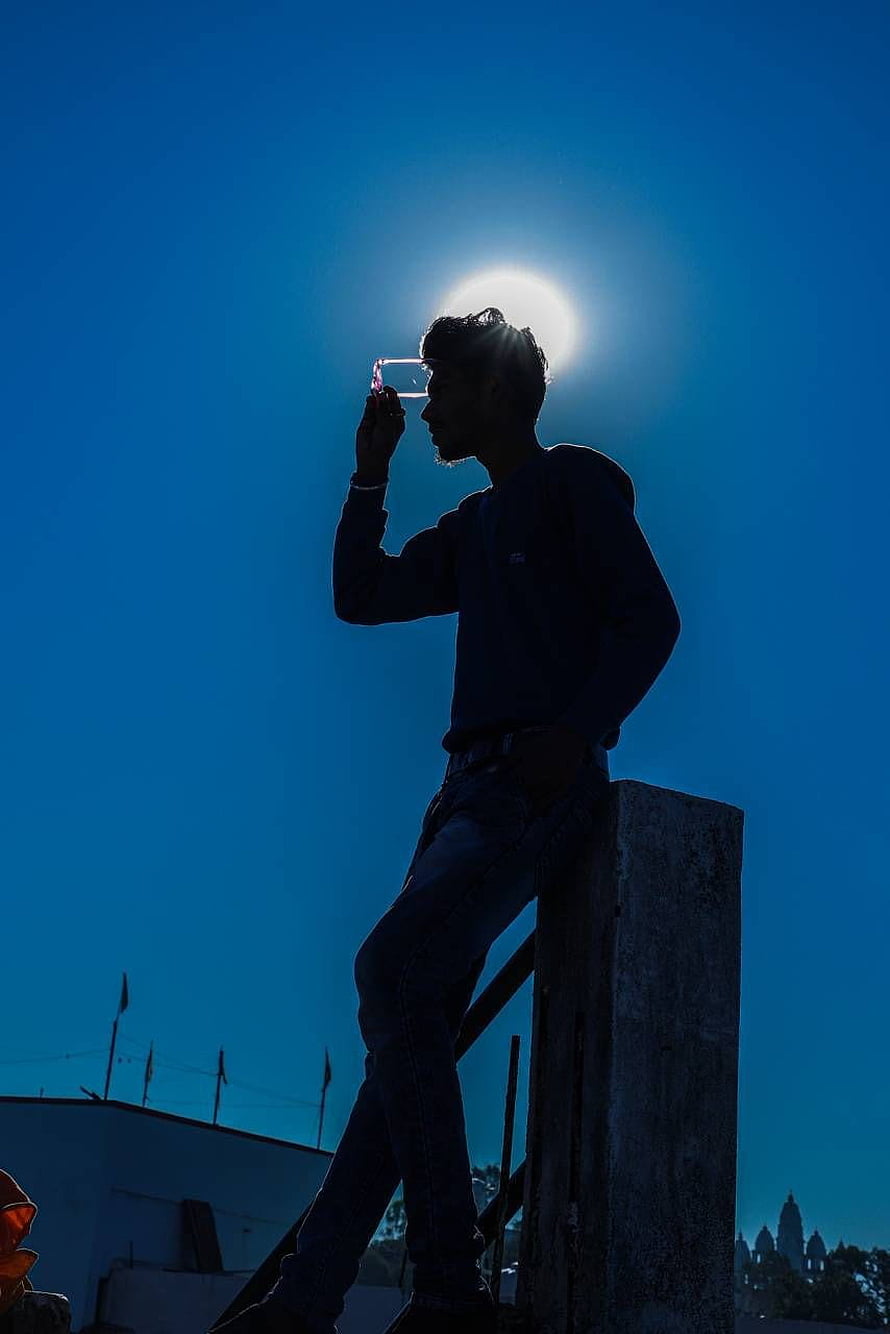 Silhouette of a young man drinking from a glass against a bright sun and deep blue sky HD phone wallpaper