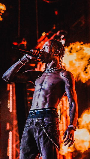 Travis Scott performing shirtless on stage with pyrotechnics and dramatic red lighting HD phone wallpaper