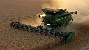John Deere X9 Combine Harvester Working in a Golden Wheat Field at Sunset HD wallpaper