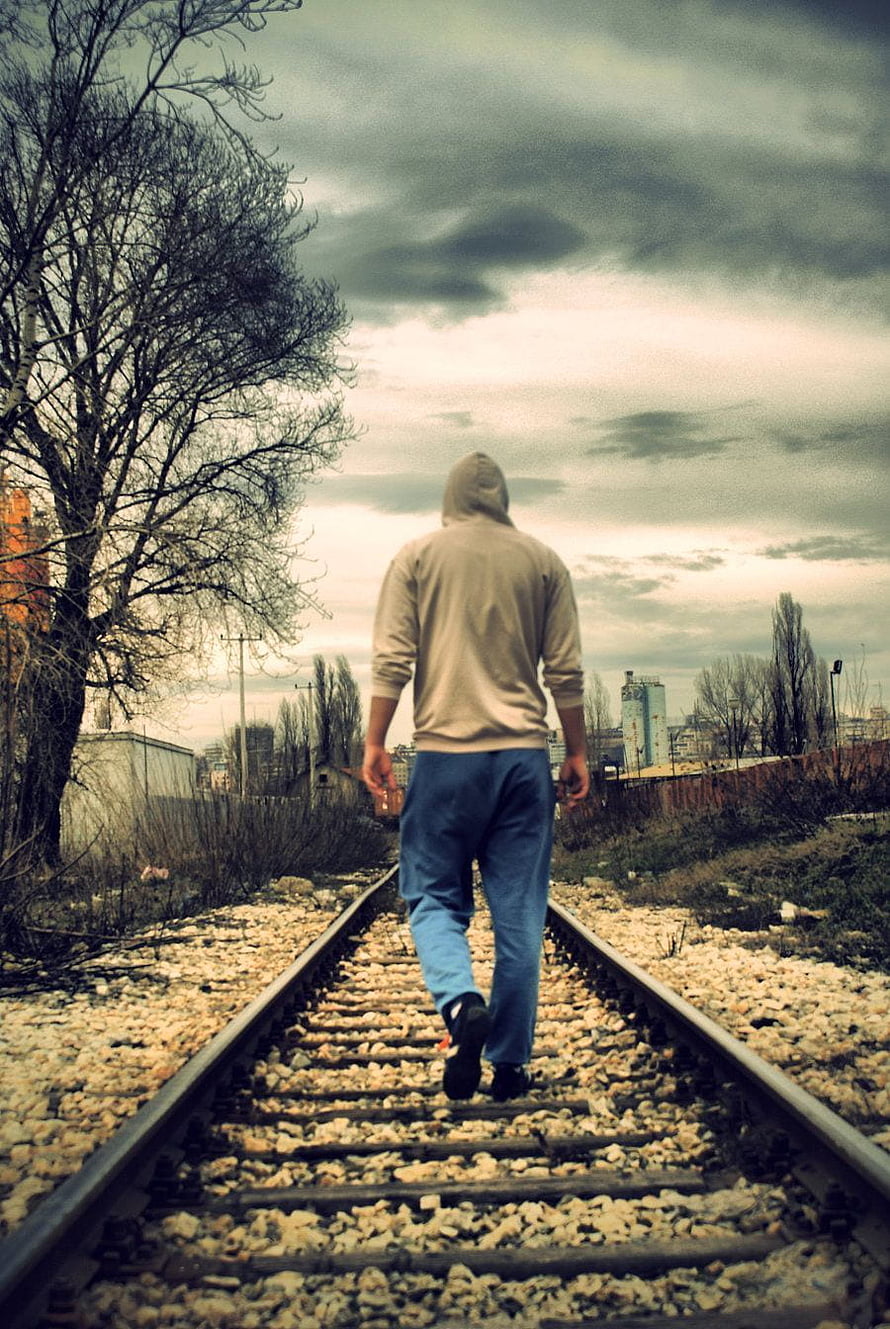 Man in Hoodie Walking Alone on Abandoned Railway Tracks Under Overcast Sky HD phone wallpaper