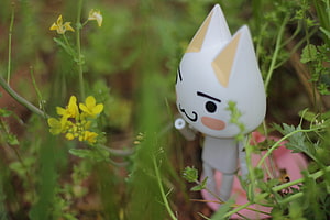 Cute White Cat Figurine in a Garden with Yellow Flowers and Green Foliage HD wallpaper