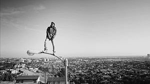 Kendrick Lamar standing on a street lamp overlooking a sprawling cityscape in black and white HD wallpaper