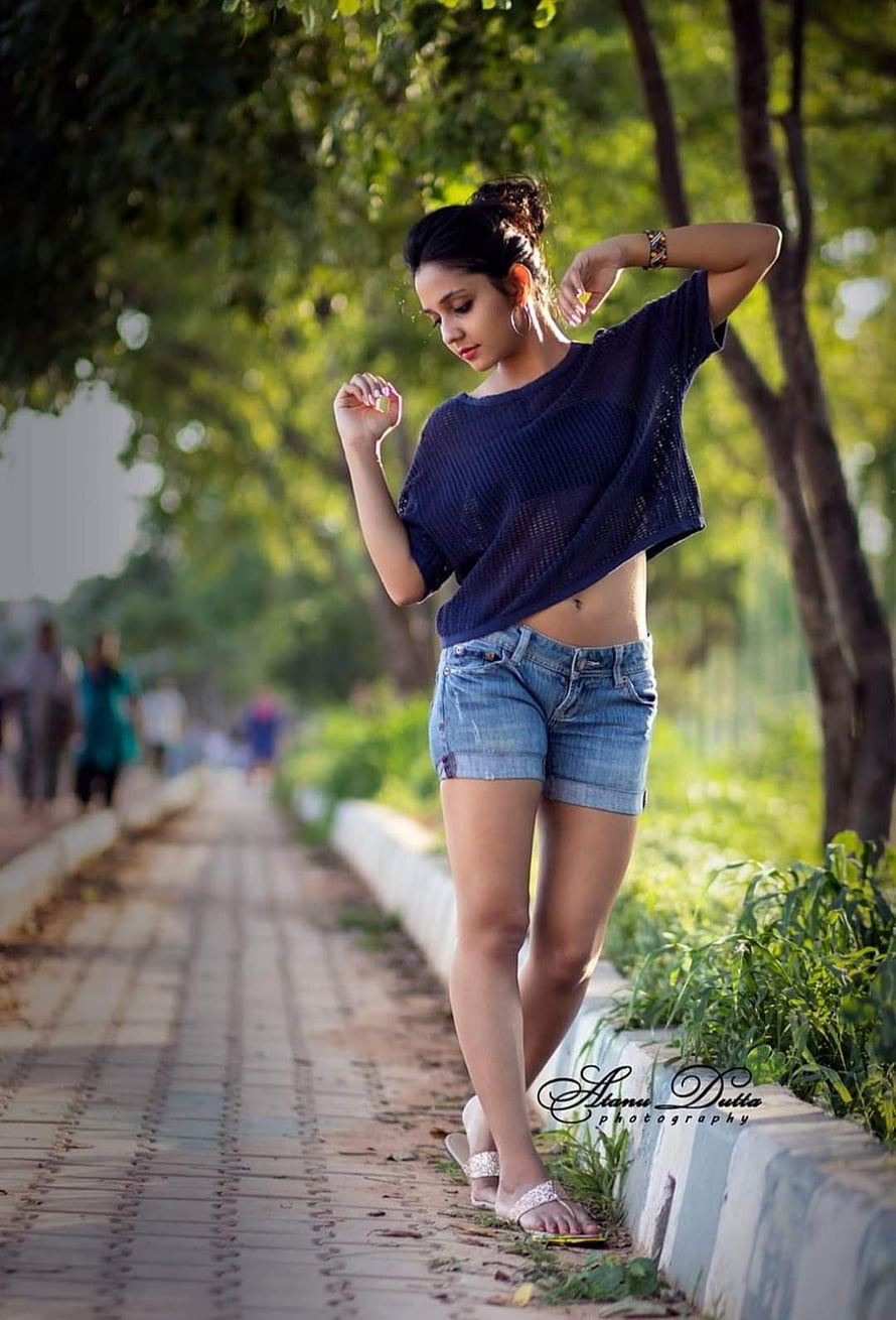 Young woman in denim shorts and navy top posing on a tree-lined park pathway HD phone wallpaper