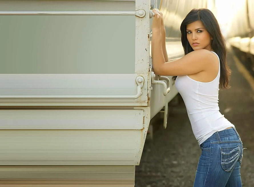 Sunny Leone in white tank top and jeans leaning against a truck HD wallpaper