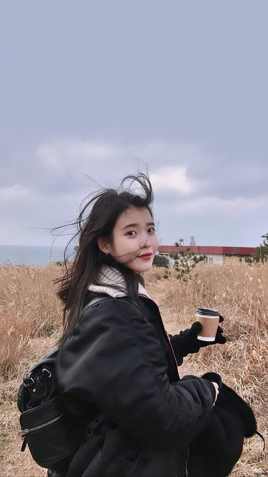 Iu in a black winter coat holding a coffee cup in a coastal field HD phone wallpaper