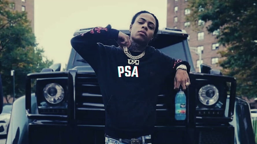 Kay Flock posing in front of a black SUV wearing a black PSA hoodie and gold chain in an urban setting HD wallpaper