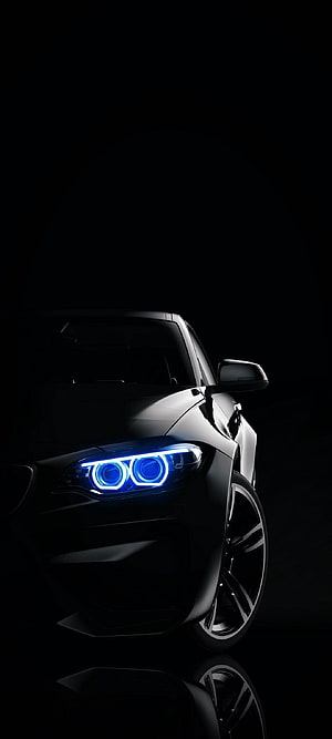 Black BMW M4 with glowing blue LED headlights in dark studio setting HD phone wallpaper
