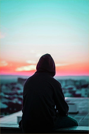 Silhouette of a person in a hoodie sitting on a rooftop watching a colorful sunset over a city skyline HD phone wallpaper