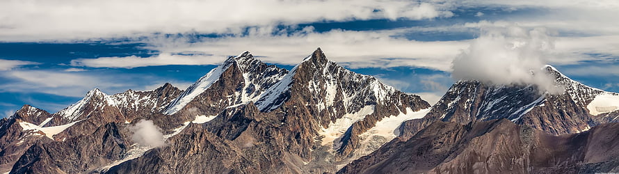 Majestic Snow-Capped Mountain Range Under a Dramatic Cloudy Sky HD wallpaper