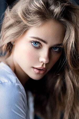 Close-up portrait of a young woman with striking blue eyes and wavy blonde hair HD phone wallpaper