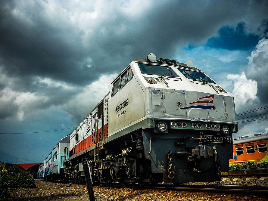 Indonesian diesel locomotive pulling passenger cars under a dramatic stormy sky HD wallpaper