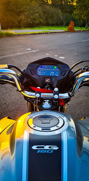 Close-up of a Honda CG 160 motorcycle dashboard and fuel tank in golden hour light HD phone wallpaper