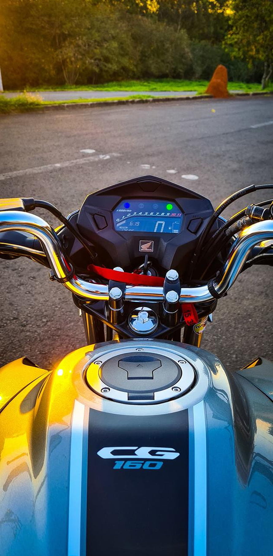 Close-up of a Honda CG 160 motorcycle dashboard and fuel tank in golden hour light HD phone wallpaper