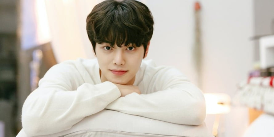 Song Kang in a White Sweater Leaning on a Cushion in a Bright Indoor Setting HD wallpaper