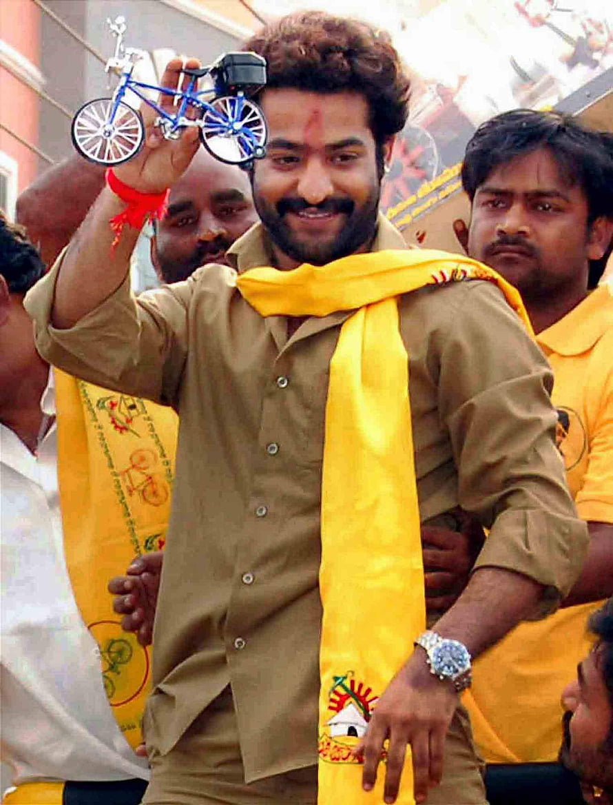 Junior NTR holding miniature bicycle at TDP political event with yellow scarf HD phone wallpaper