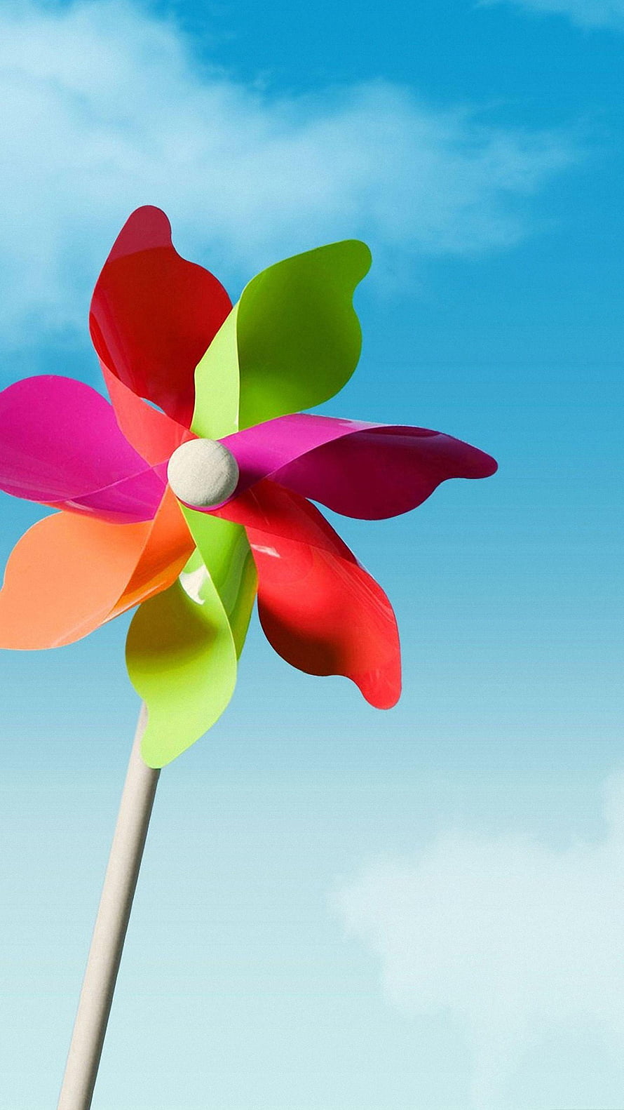 Colorful Pinwheel Spinning Against a Bright Blue Sky with Soft White Clouds HD phone wallpaper