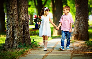 Young boy and girl holding hands while walking through a sunlit park with red roses HD wallpaper