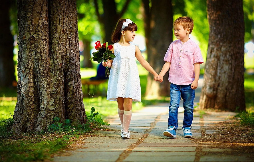 Young boy and girl holding hands while walking through a sunlit park with red roses HD wallpaper