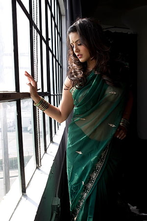 Sunny Leone in an elegant emerald green saree with gold embroidery standing by a window HD phone wallpaper